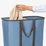 Person placing a towel into a blue laundry basket with a white background