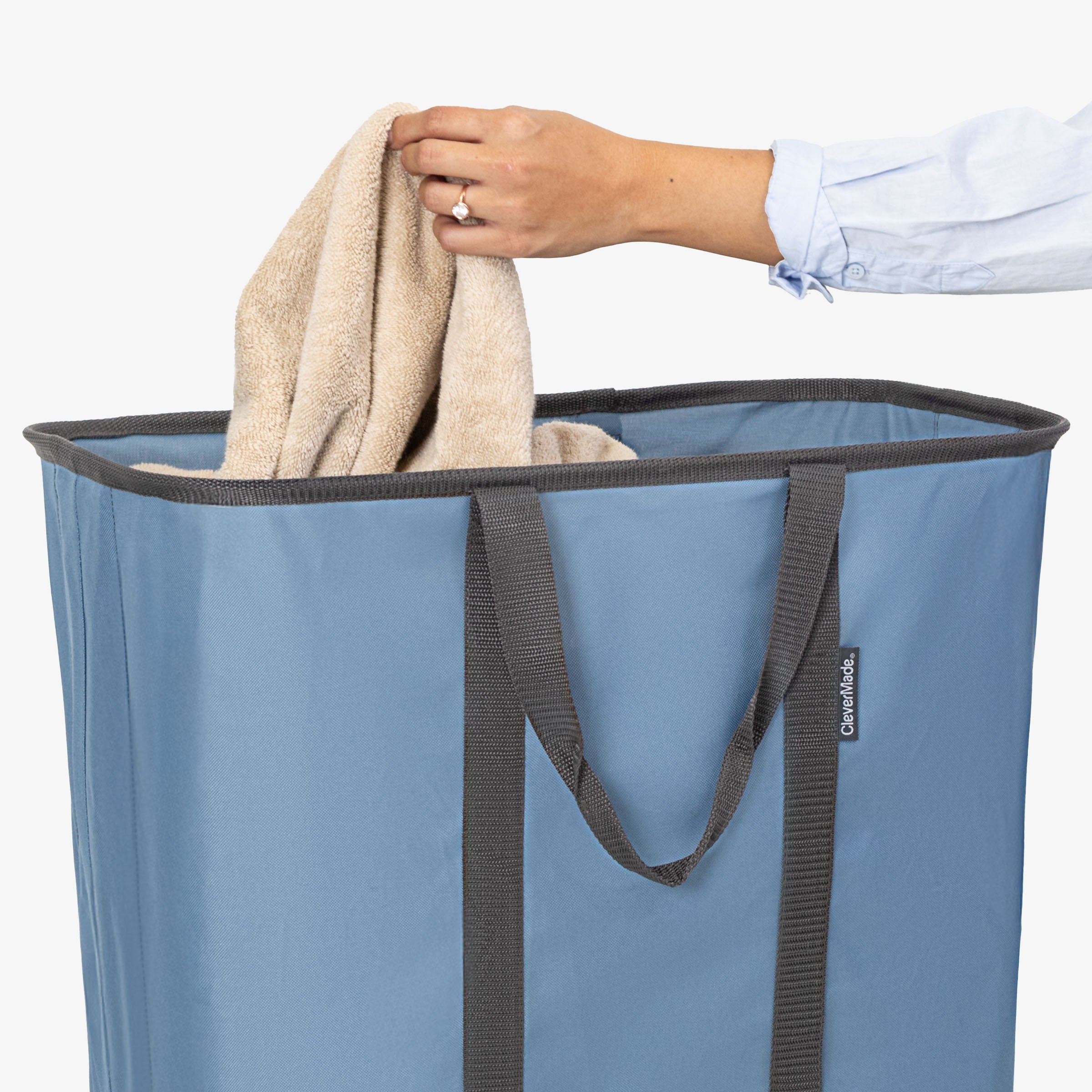 Person placing a towel into a blue laundry basket with a white background