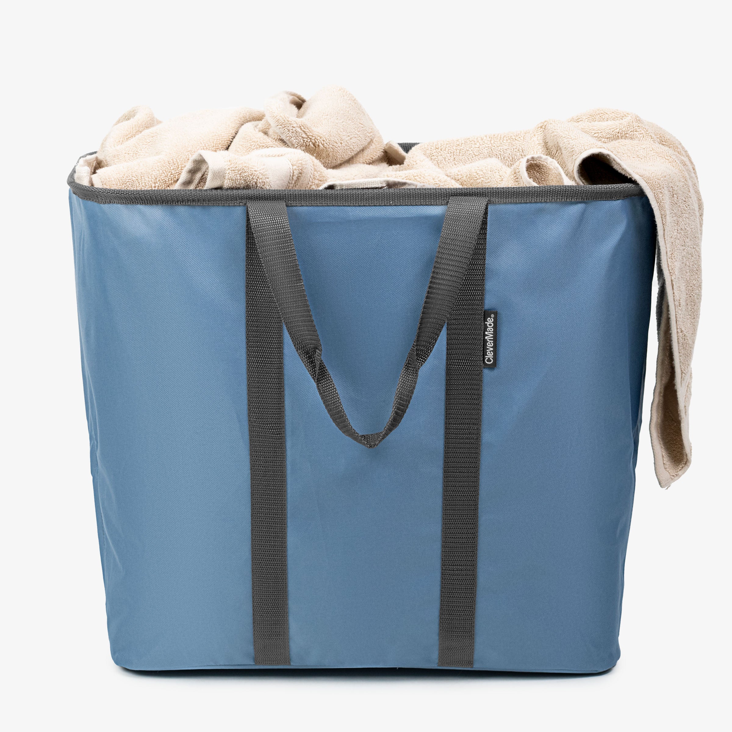 Blue laundry caddy with black handles filled with beige towels on a white background