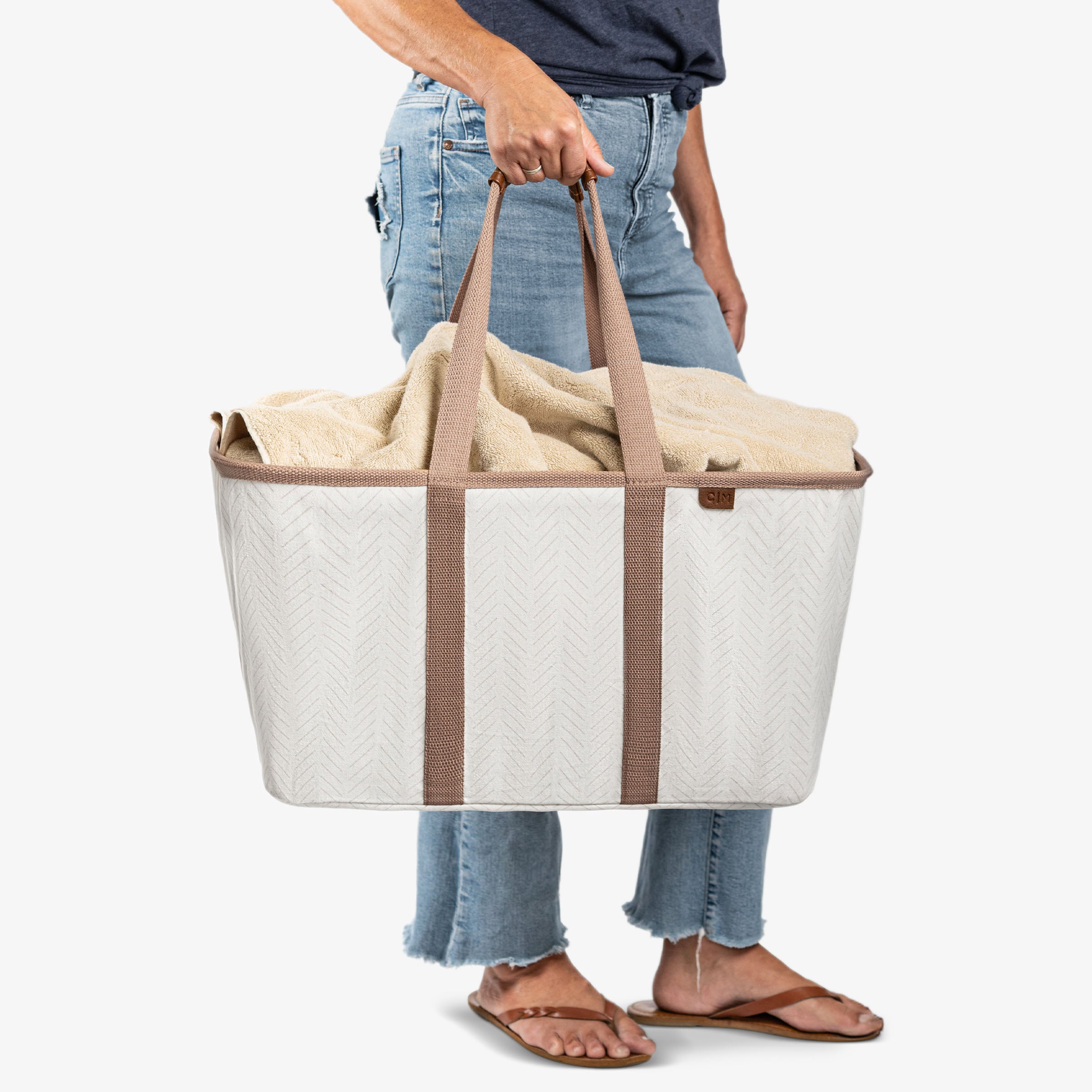 Person holding a large beige tote bag with brown straps on a white background