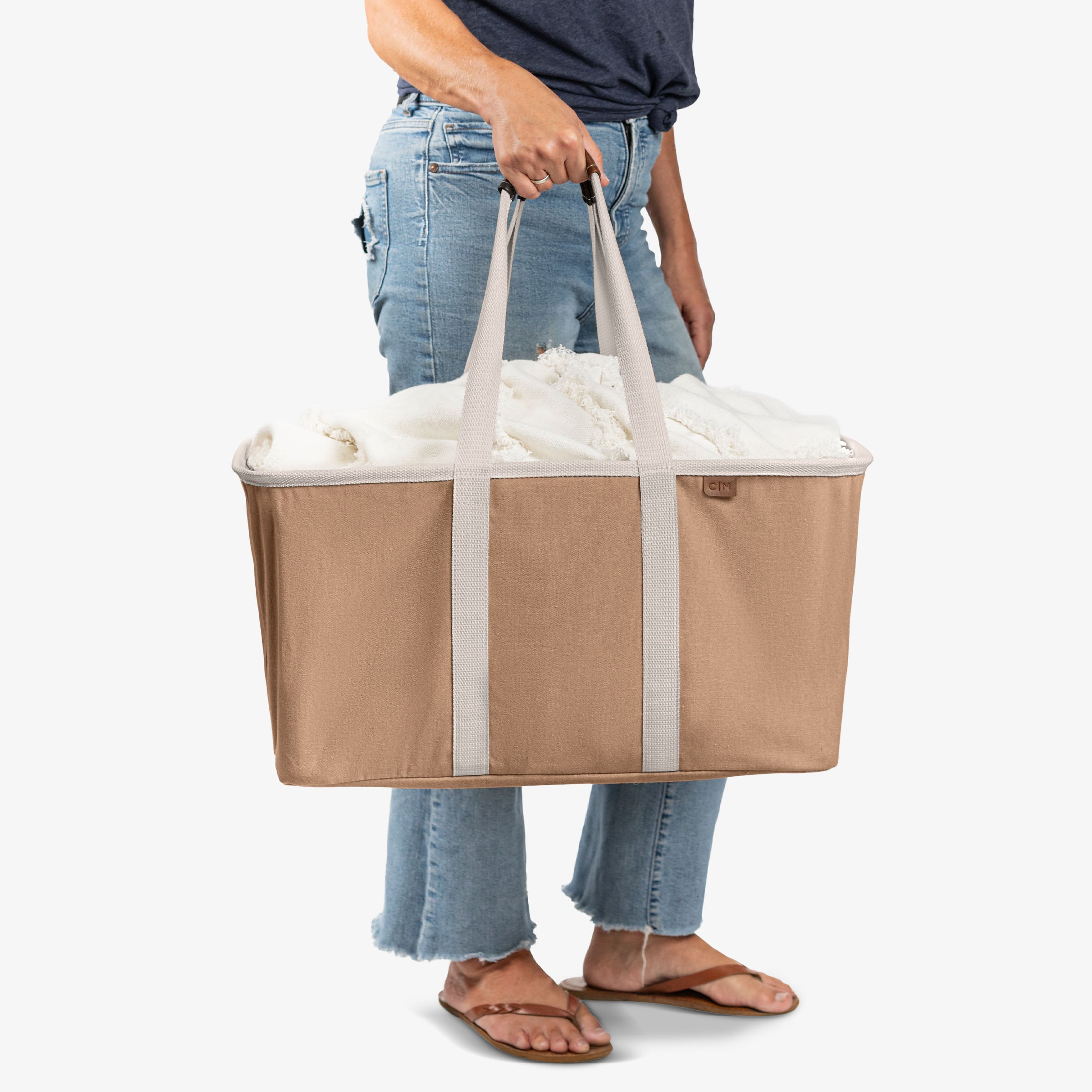 Person holding a large beige and white tote bag filled with items on a white background