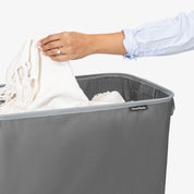 Person placing a white garment into a gray CleverMade laundry basket.
