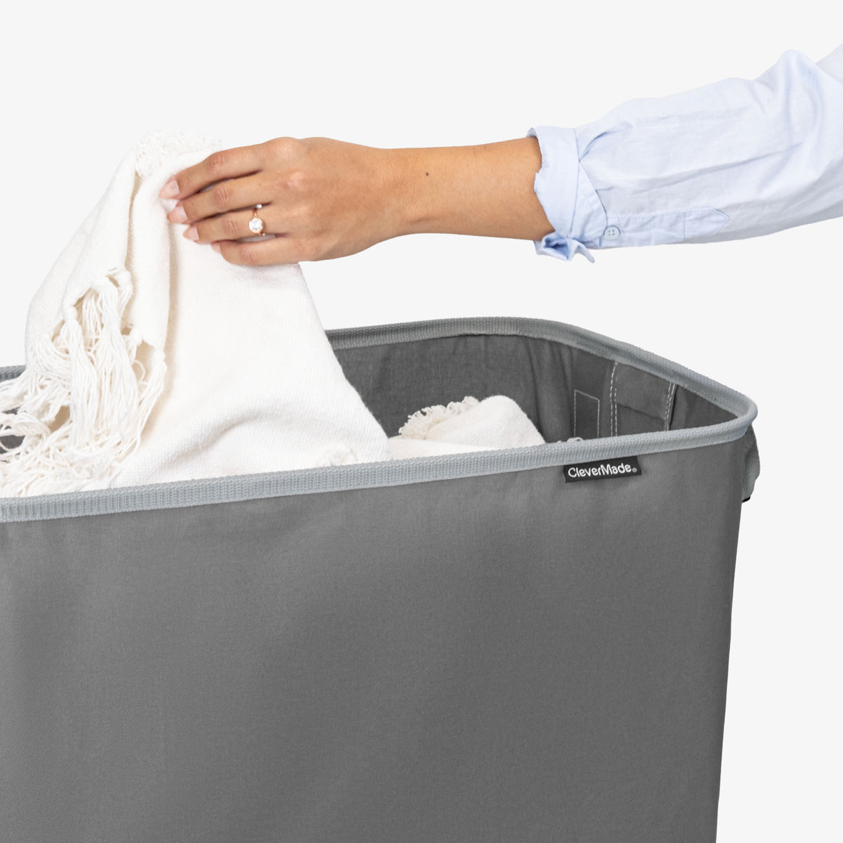 Person placing a white garment into a gray CleverMade laundry basket.