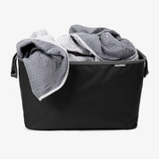 A bedsheet into a black CleverMade laundry basket.