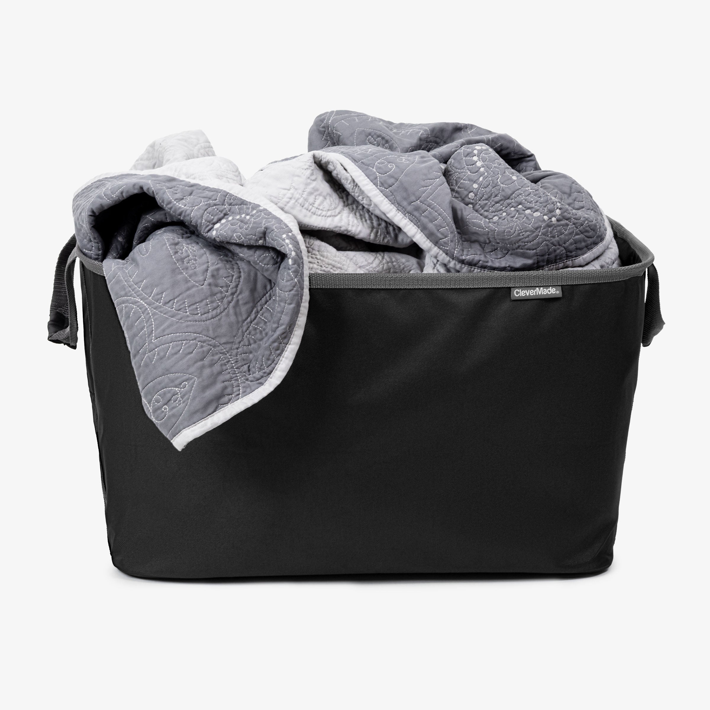 A bedsheet into a black CleverMade laundry basket.