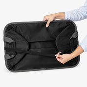Person holding a black collapsible laundry basket with gray straps on a white background
