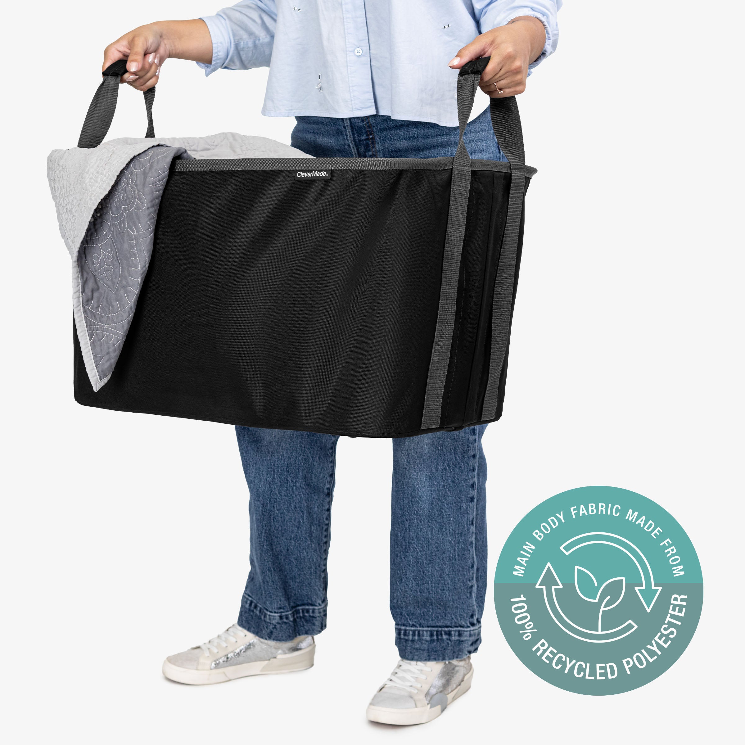 Person holding a black and gray collapsible laundry basket with a visible recycling logo on a white background