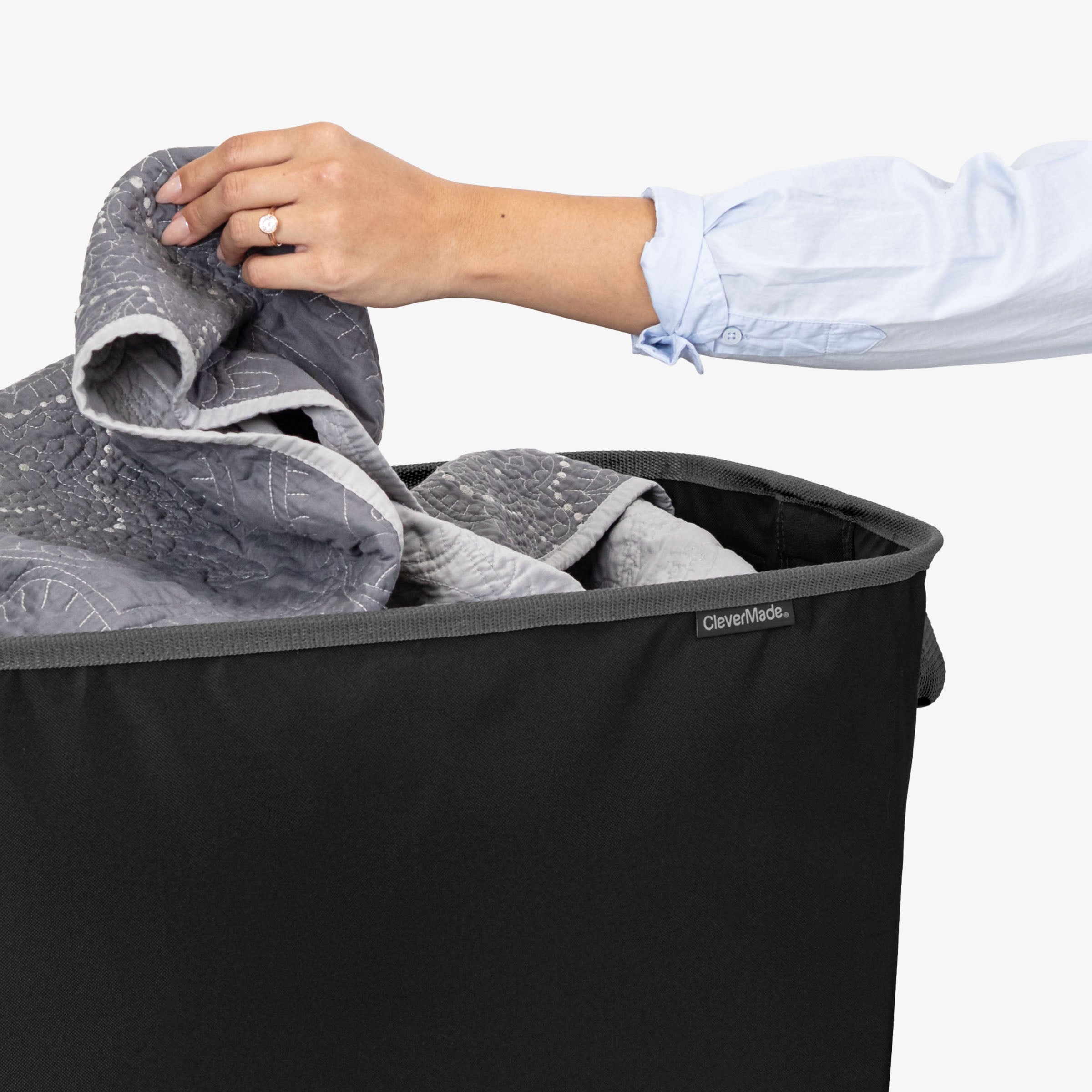 Person placing a bedsheet into a black CleverMade laundry basket.