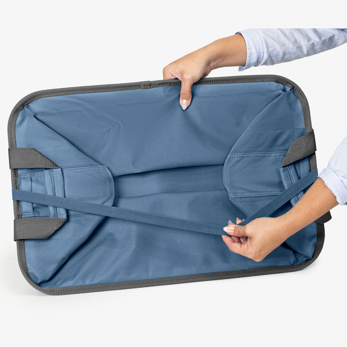 Blue collapsible laundry basket with gray straps held by a person on a white background