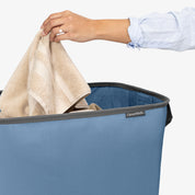 Person placing a towel into a blue CleverMade laundry basket.