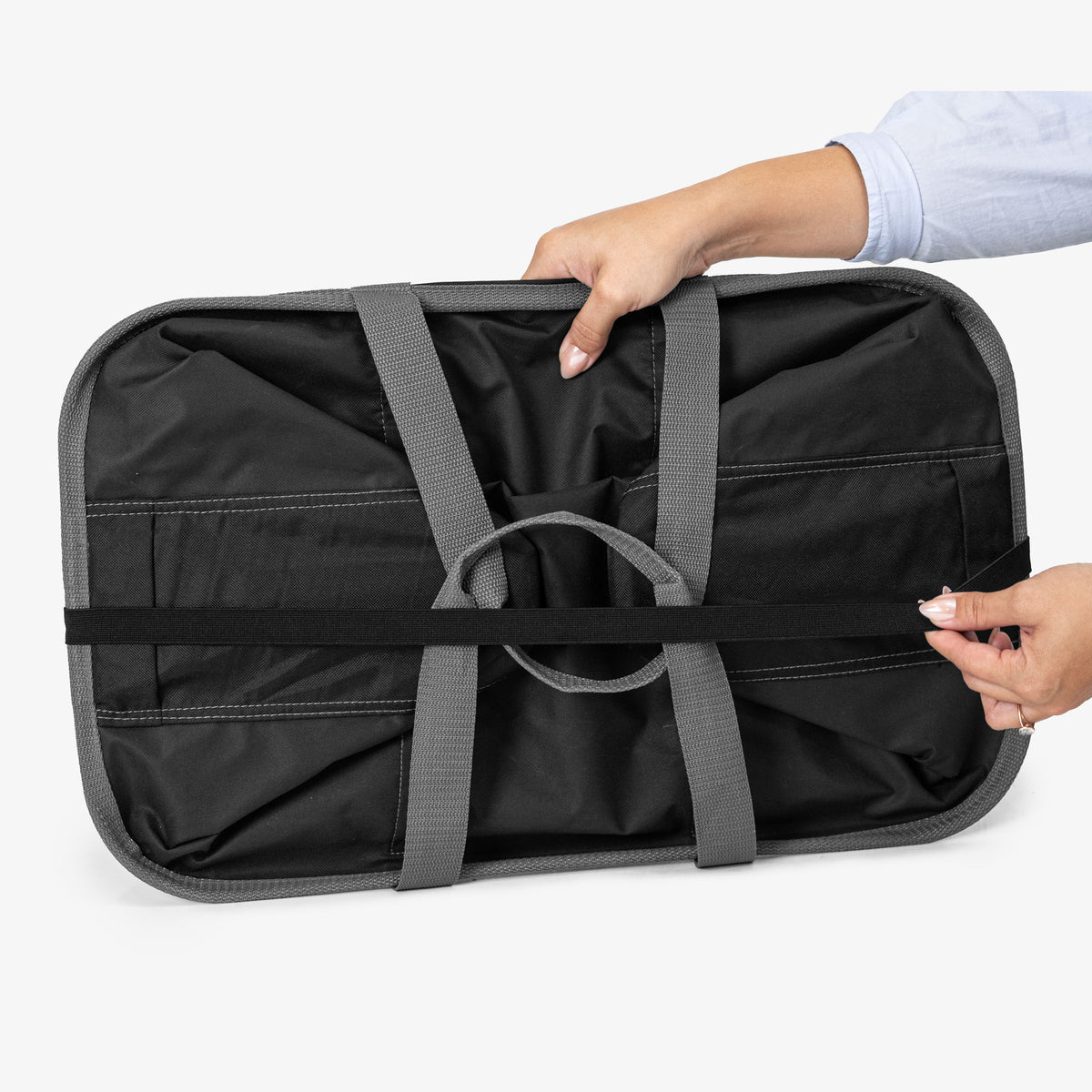Black laundry tote bag with gray straps being held by a person on a white background