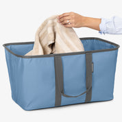 Blue laundry tote with gray handles being used to hold a beige towel.