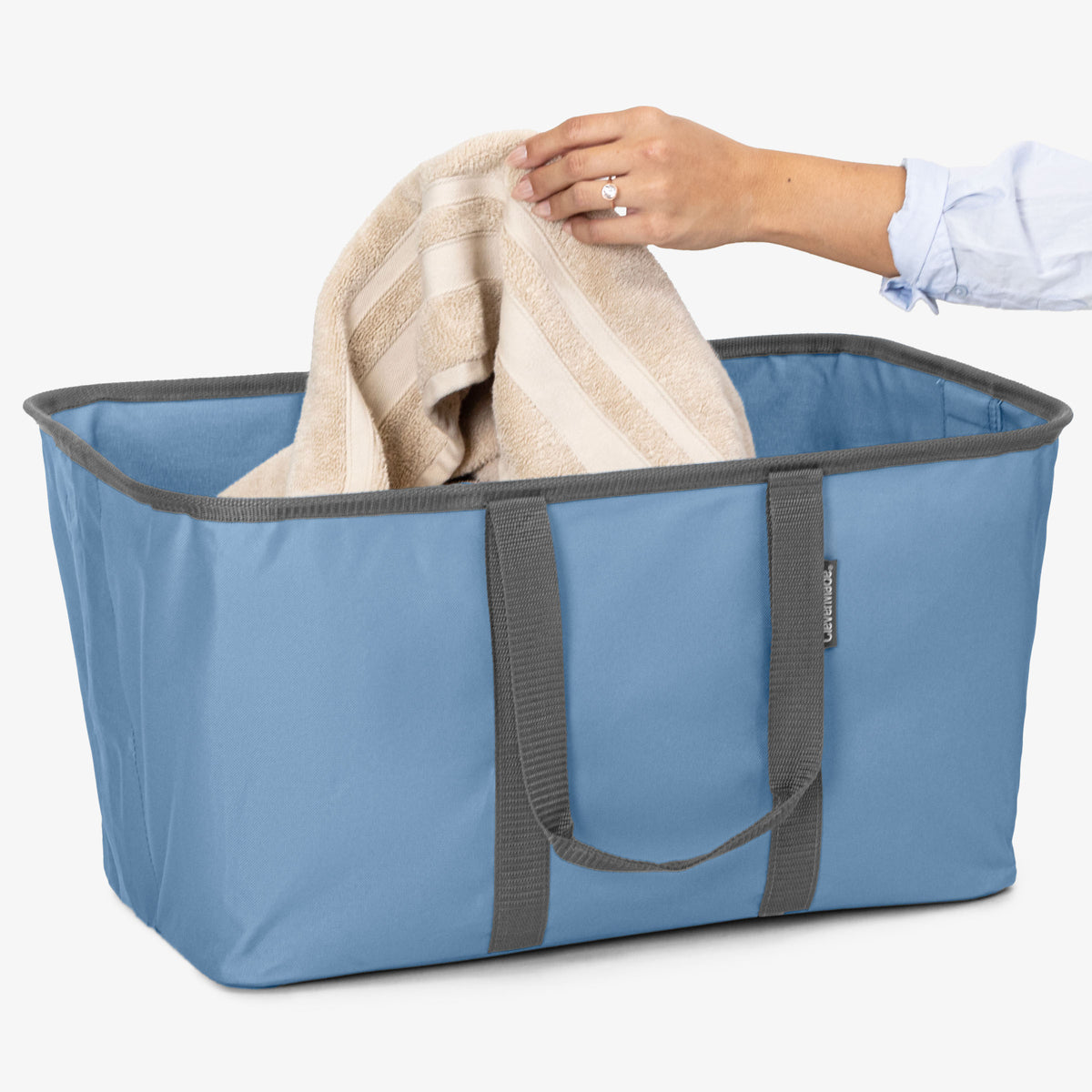 Blue laundry tote with gray handles being used to hold a beige towel.
