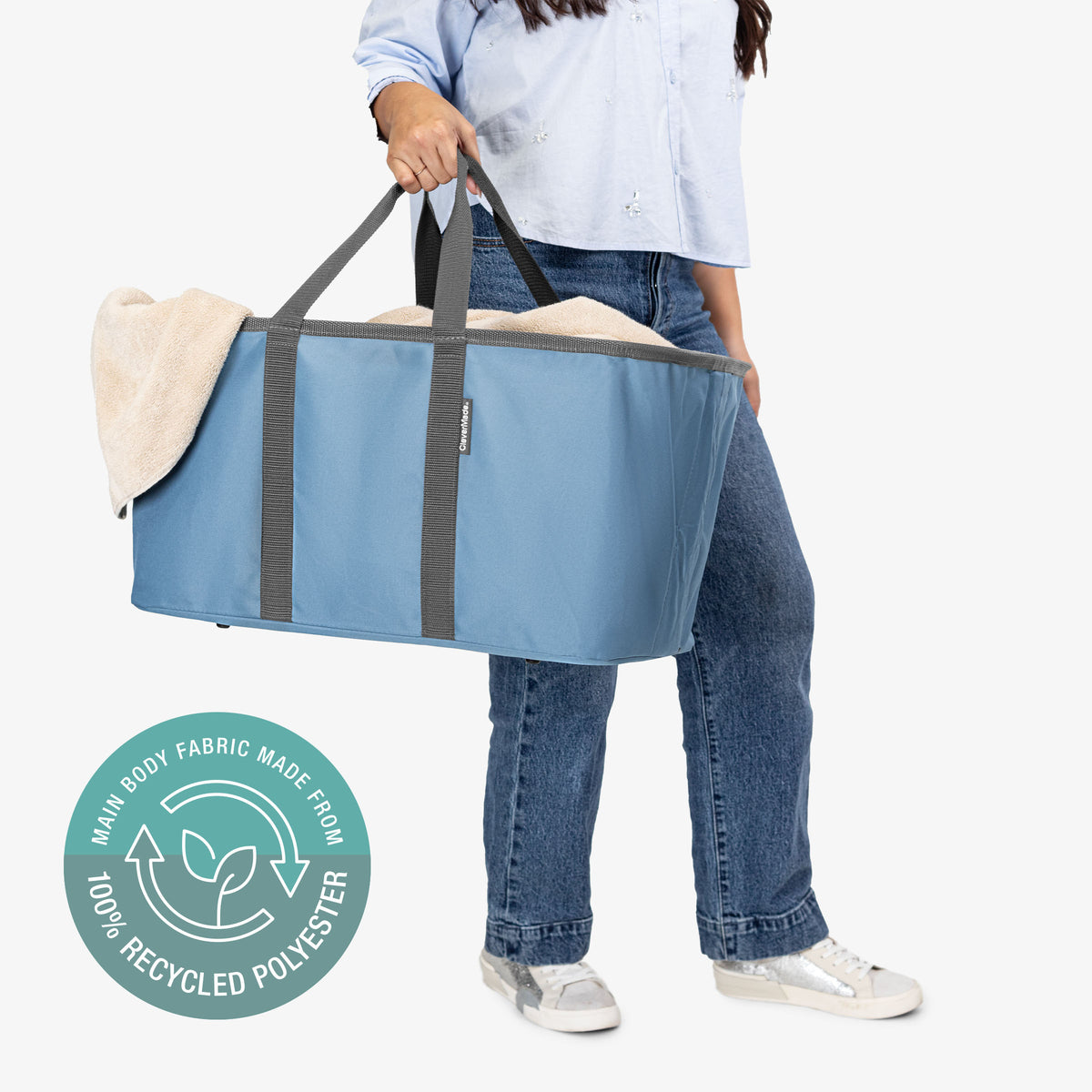 Person holding a large blue laundry tote bag with a visible brand logo on a white background