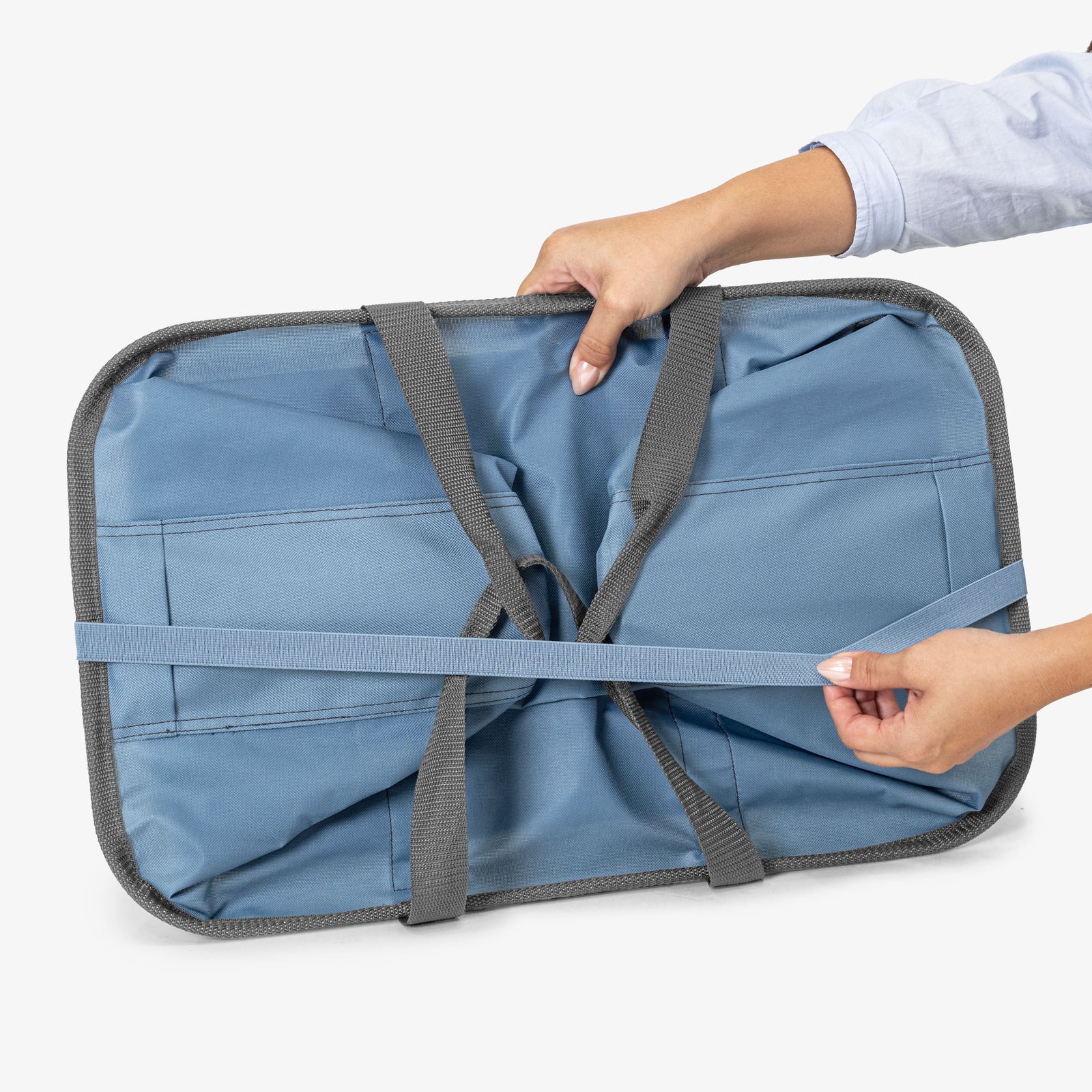 Blue laundry tote bag with straps being adjusted by a person on a white background