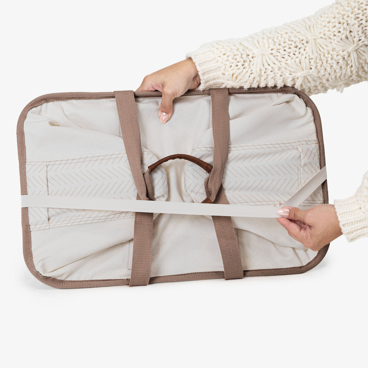 Person holding a cream collapsible laundry basket LUXE with brown straps on a white background