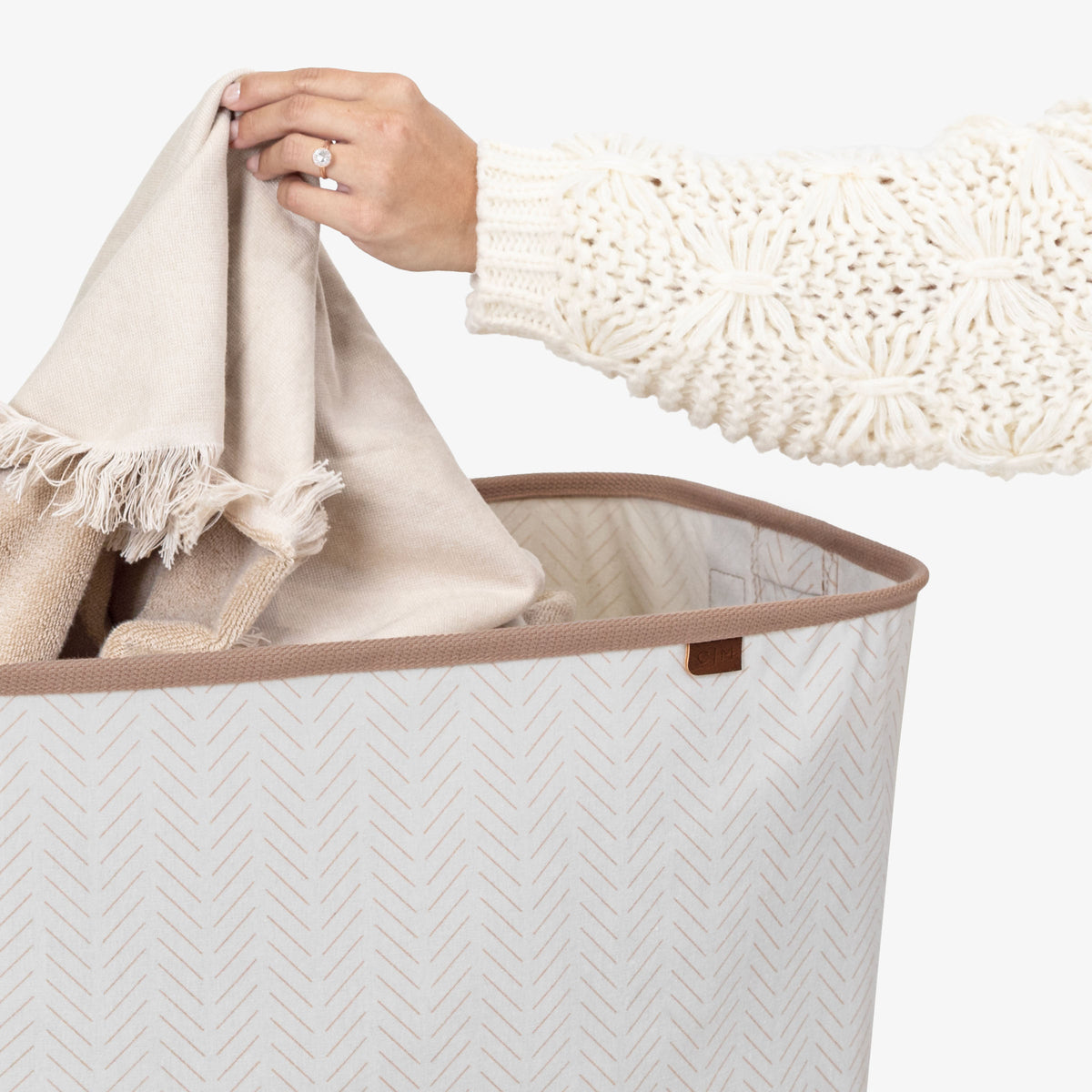 Person placing a beige towel into a cream collapsible laundry basket LUXE
 on a light background