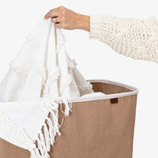 Person holding a white towel with fringe over a beige laundry basket.