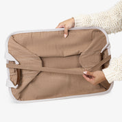Person holding a folded beige collapsible laundry basket LUXE with cream straps on a white background