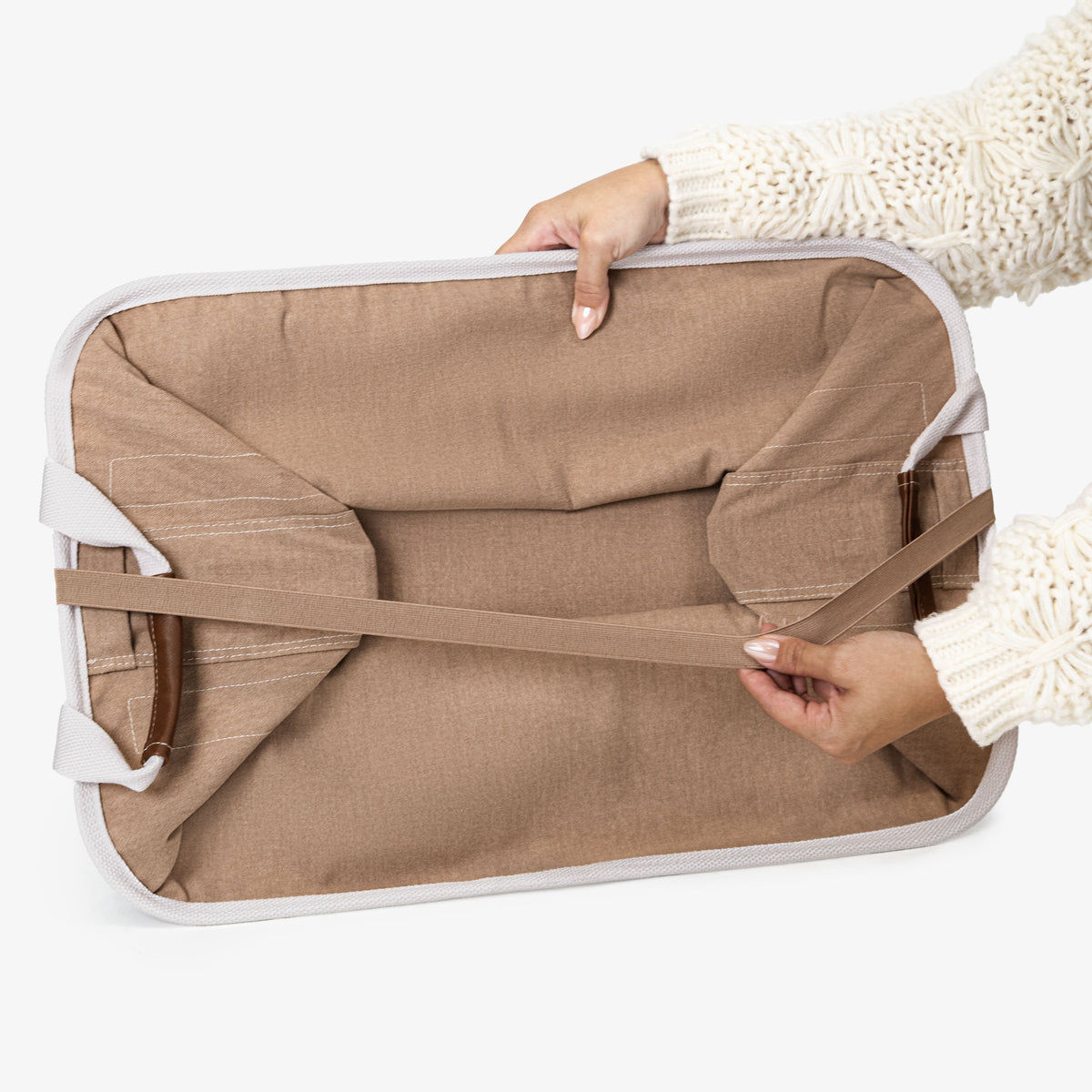 Person holding a folded beige collapsible laundry basket LUXE with cream straps on a white background