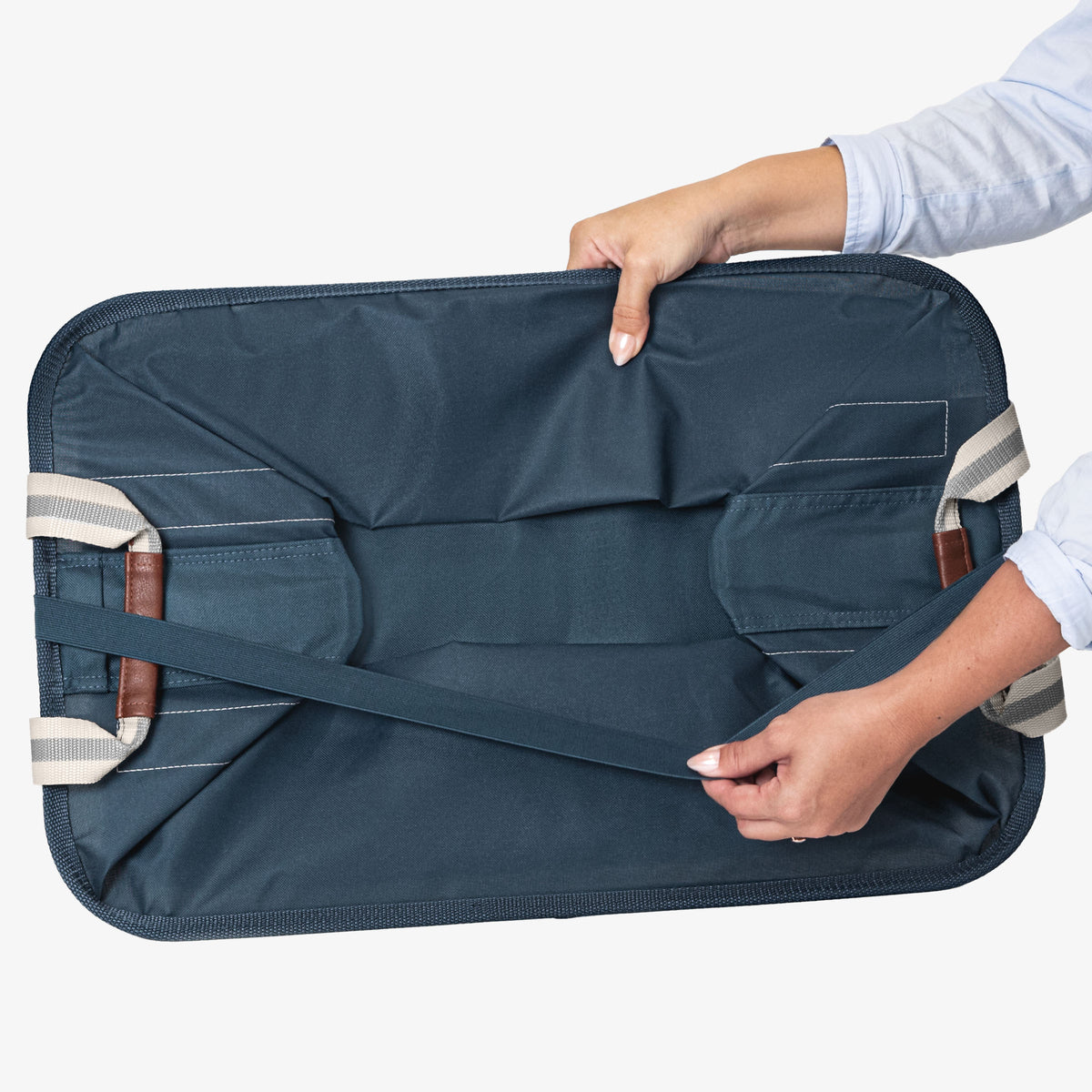 Person holding a navy blue collapsible laundry basket with straps on a white background