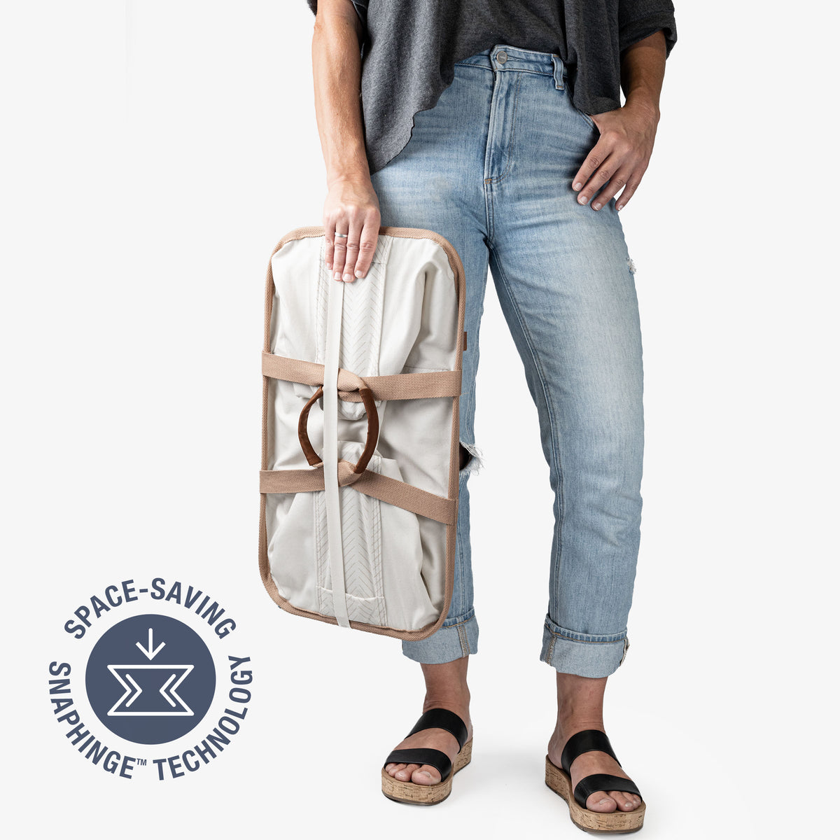 Person holding a beige laundry caddy LUXE bag with space-saving snap hinge technology label.