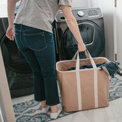 Person holding a large brown tote bag in front of a washing machine