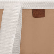 Close-up of a laundry caddy LUXE bag with a brown label featuring 'C|M' on a beige and white textured background.