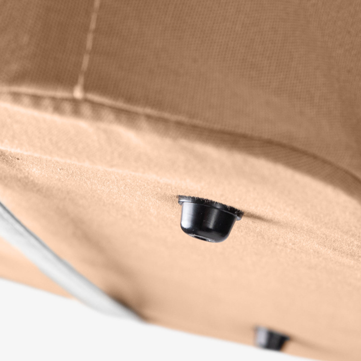 Close-up of a black button foot of a beige fabric surface