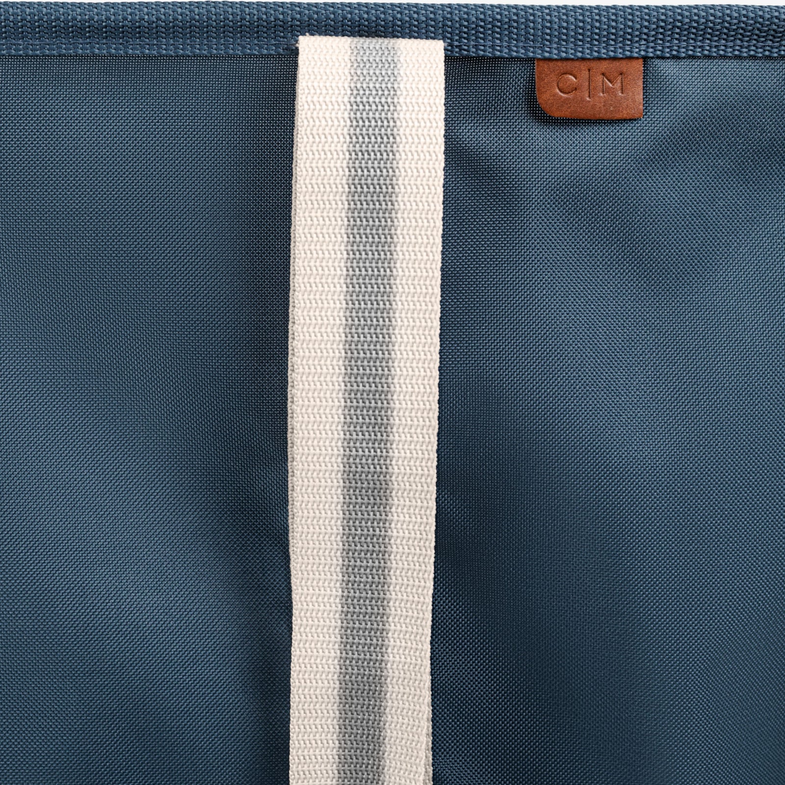 Close-up of a blue bag with a white strap and a brown leather patch with 'C|M' branding.