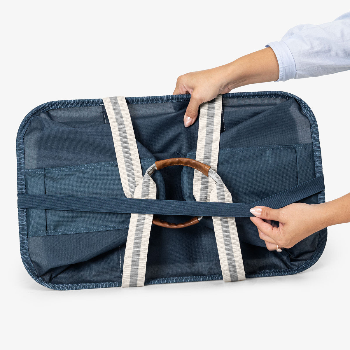 Navy blue bag with a brown handle held by a person on a white background