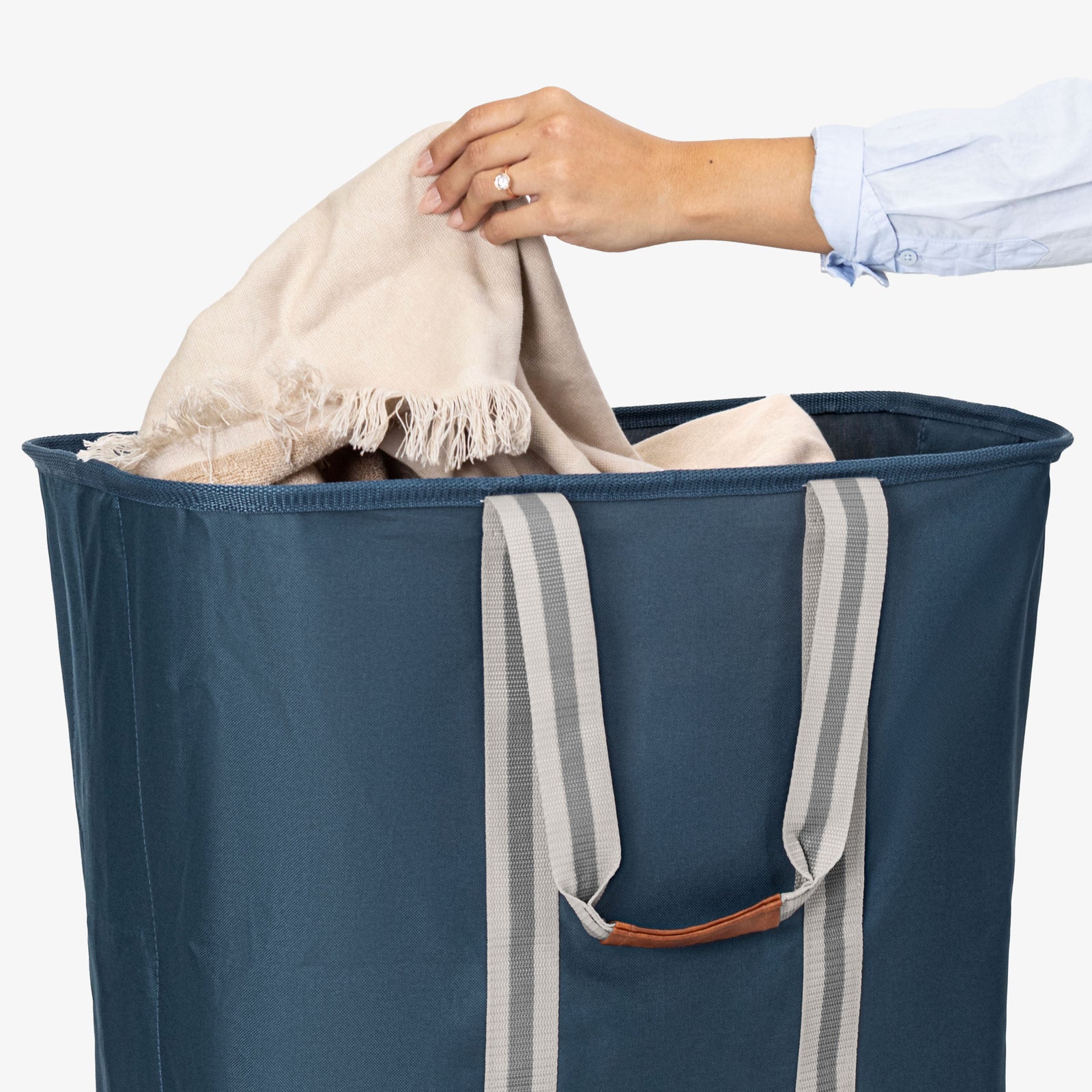 Person placing a beige towel into a blue laundry bag on a white background