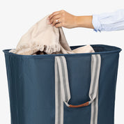 Person placing a beige towel into a blue laundry bag on a white background