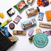 Assorted snacks and food items on a white surface with a '100% Recycled Plastic' logo.