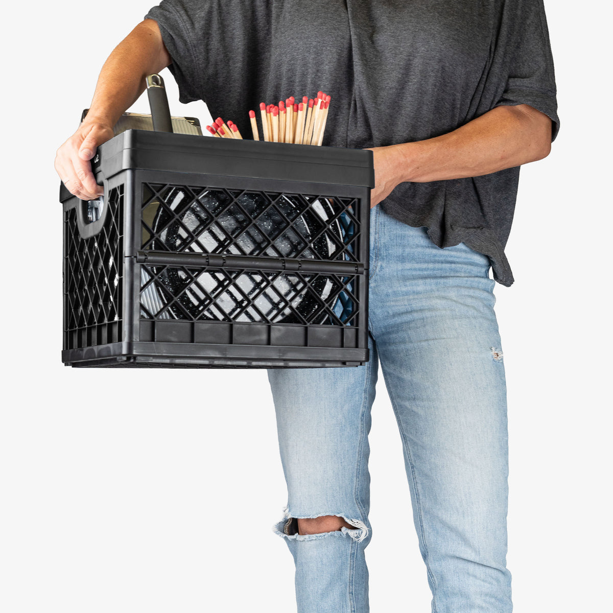 Person holding a black crate filled with items on a white background