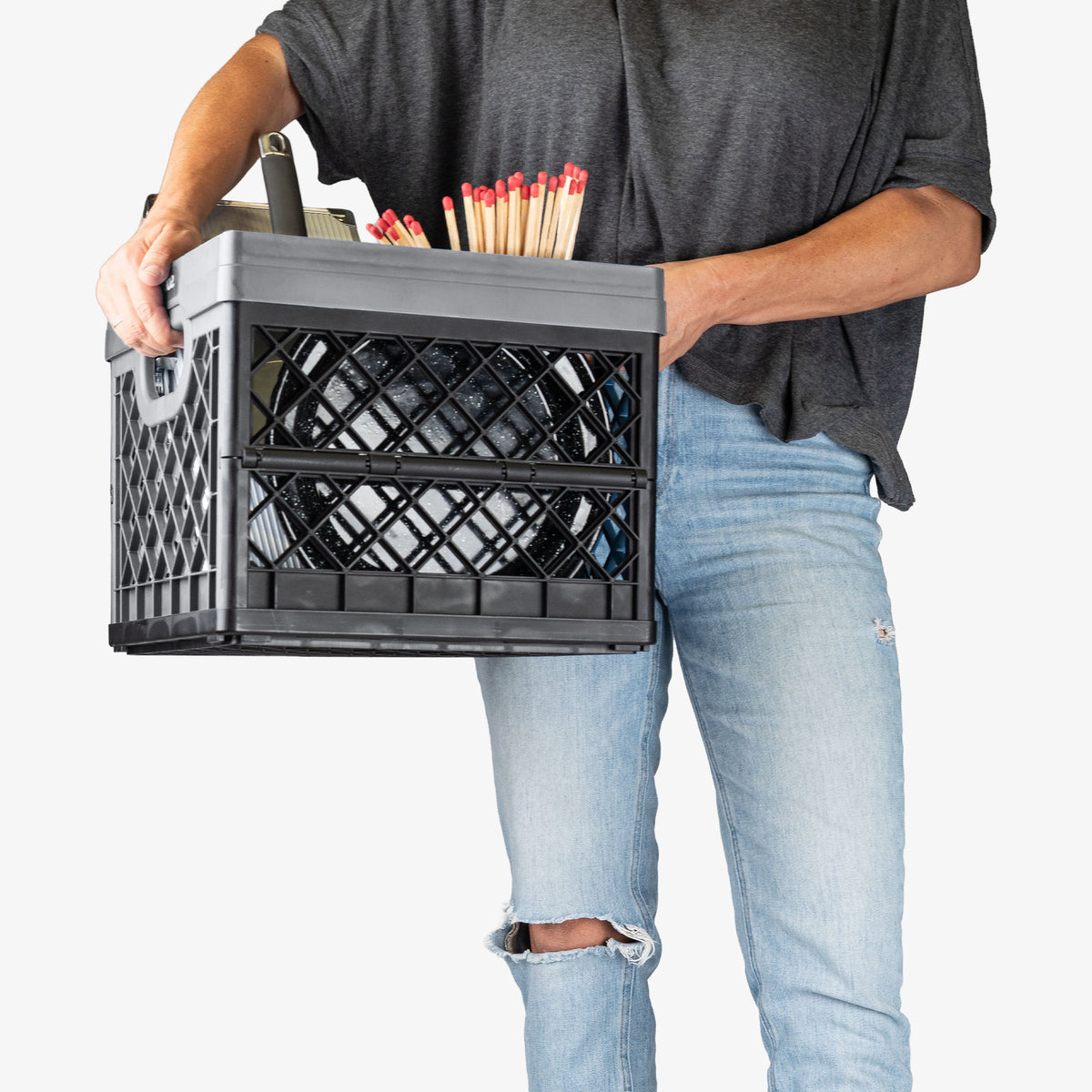 Person holding a black milk crate filled with items on a white background