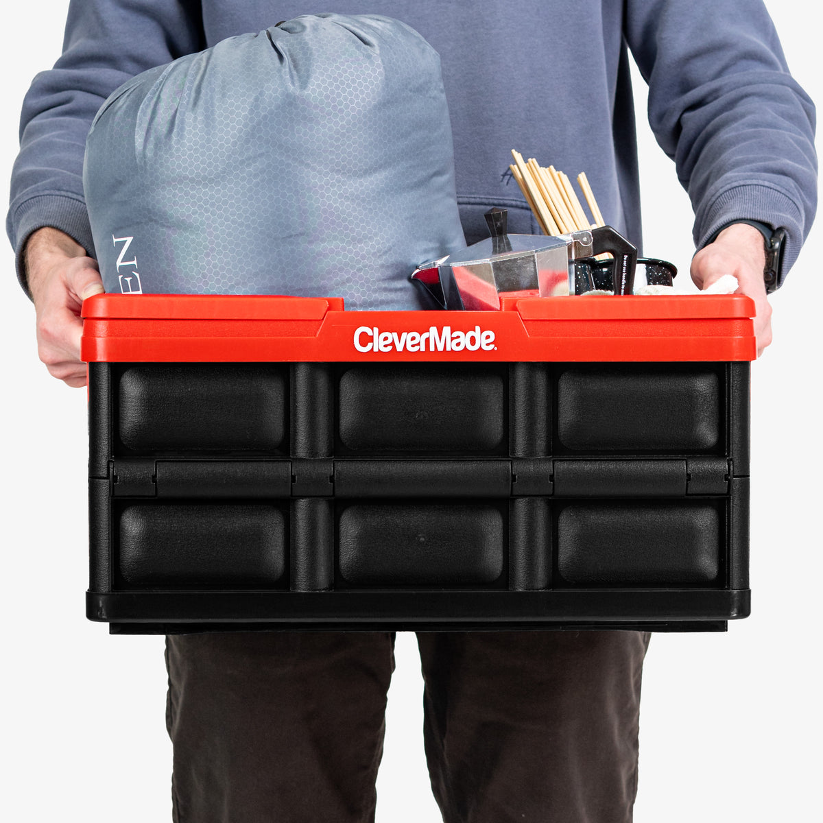 Person holding a red CleverMade collapsible basket with tools inside on a white background