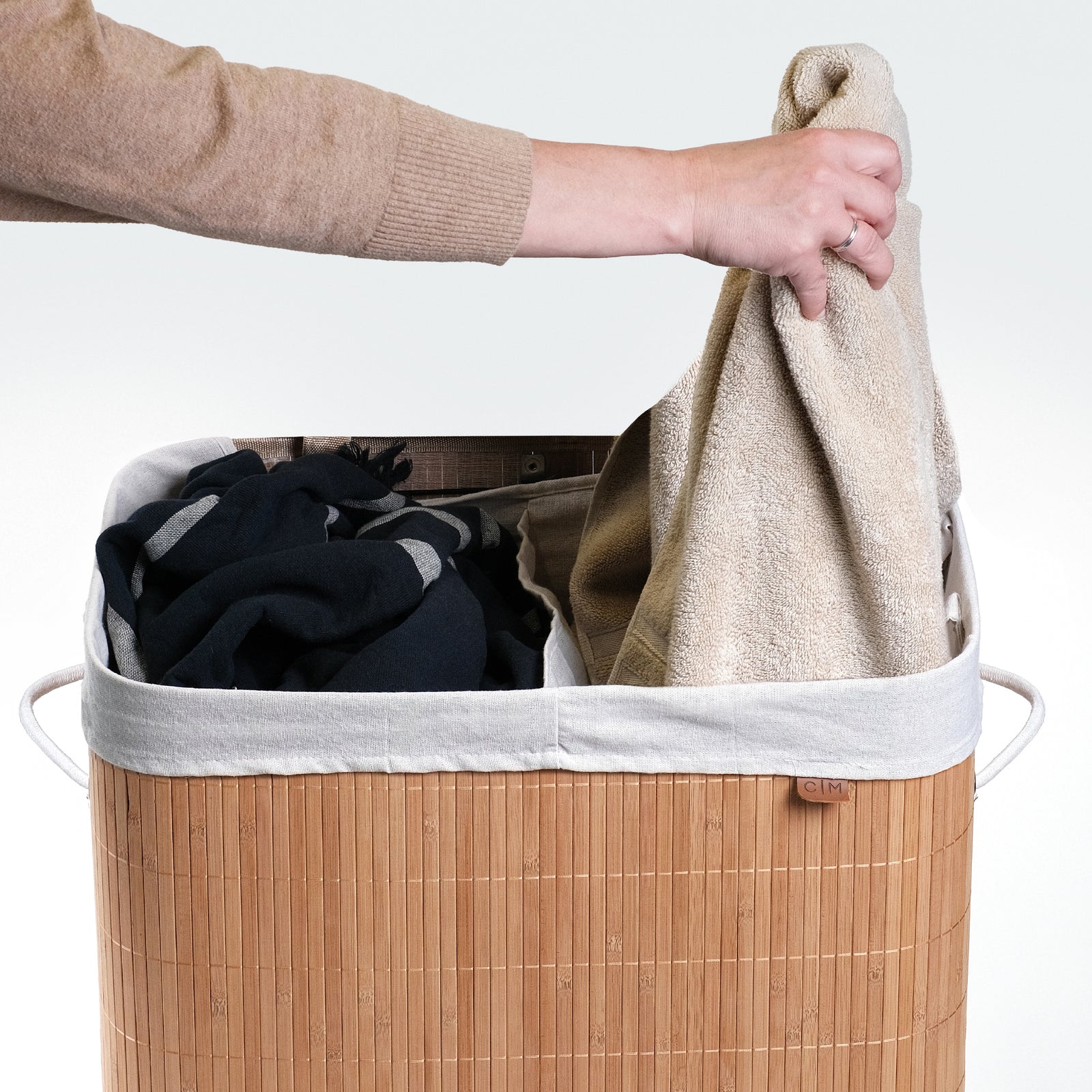 Towels are being placed at the collapsible bamboo laundry hamper