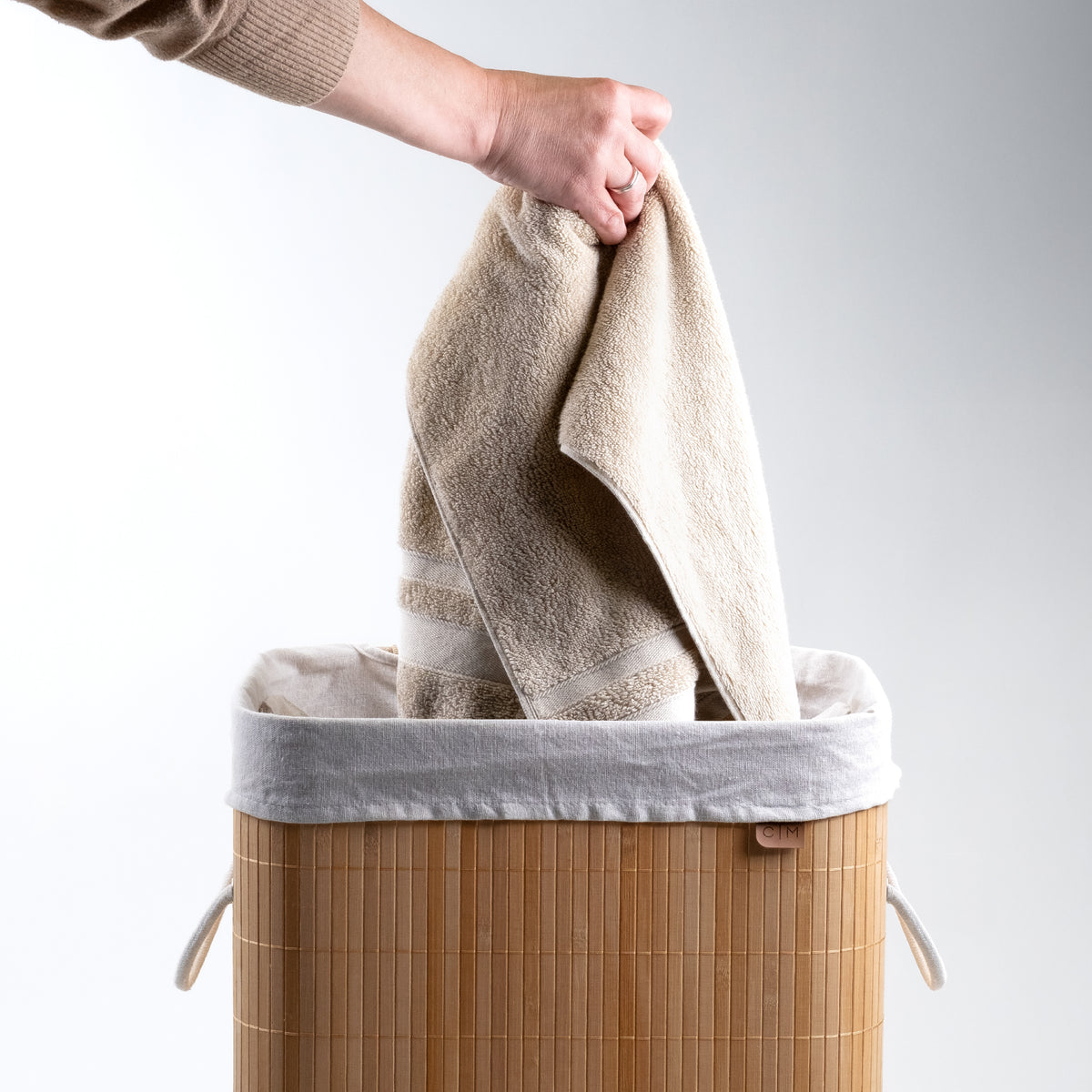 Towel being placed at the collapsible bamboo laundry hamper