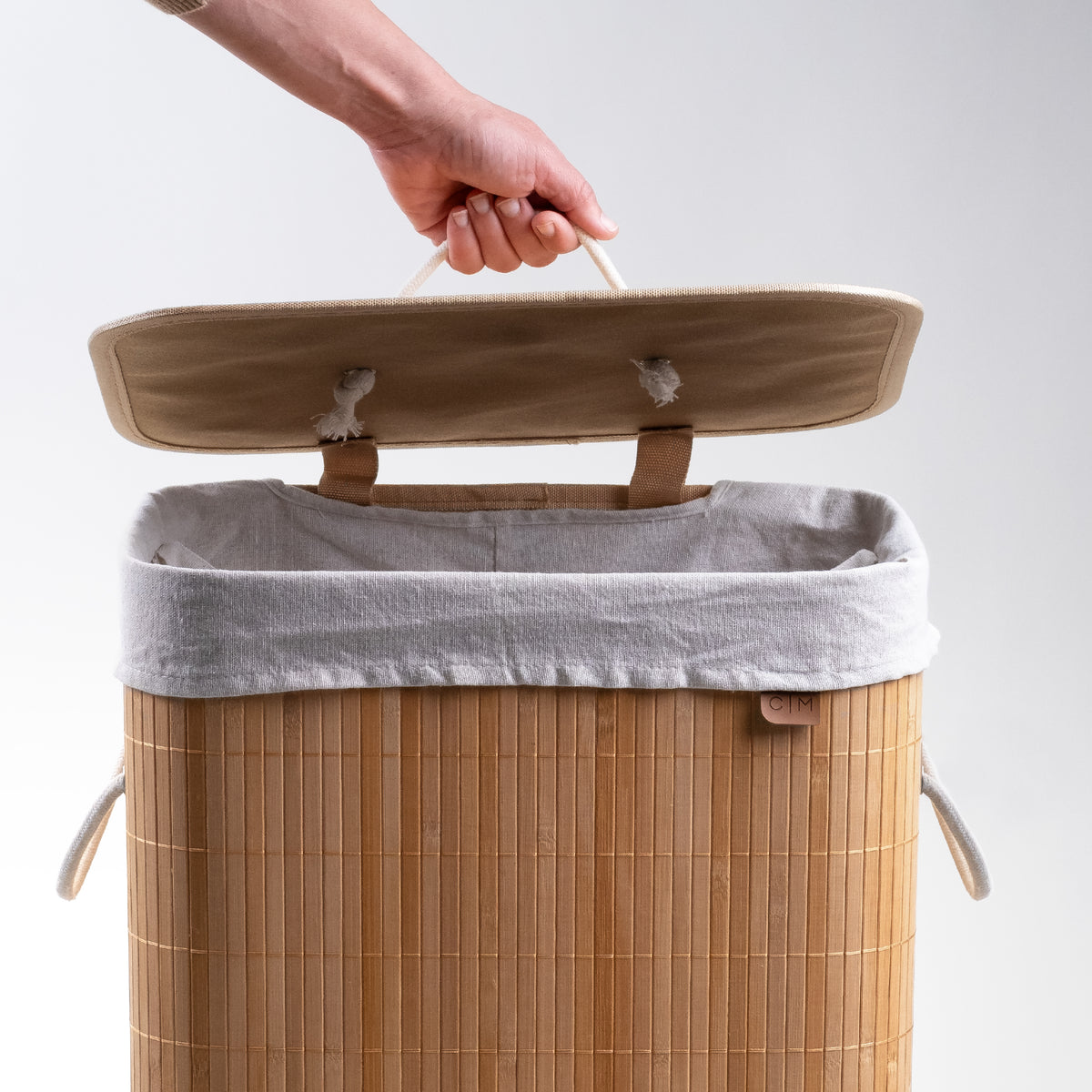 Opening cover of collapsible bamboo laundry hamper with a lid and handles, featuring a natural beige color.