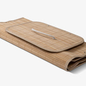 Folded collapsible bamboo laundry hamper with a lid and handles, featuring a natural beige color.