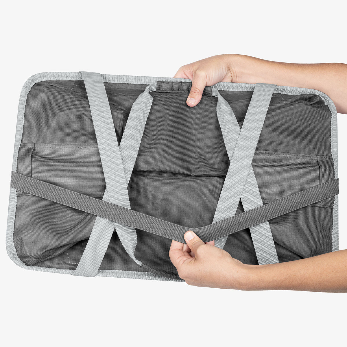 Folded Gray collapsible tote MAX with straps held by a person on a white background