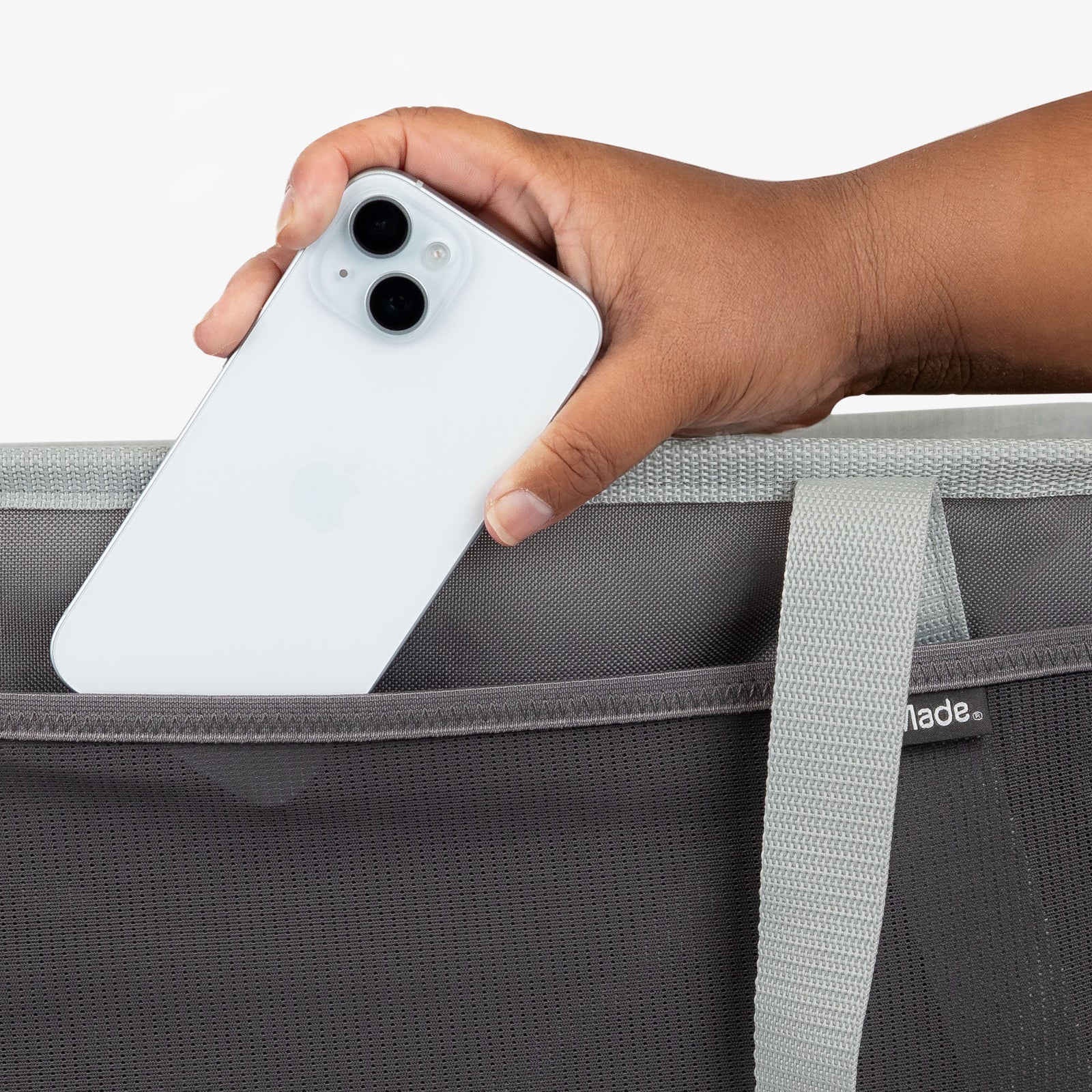 Hand holding a white phone above a gray collapsible tote bag with a visible brand logo.