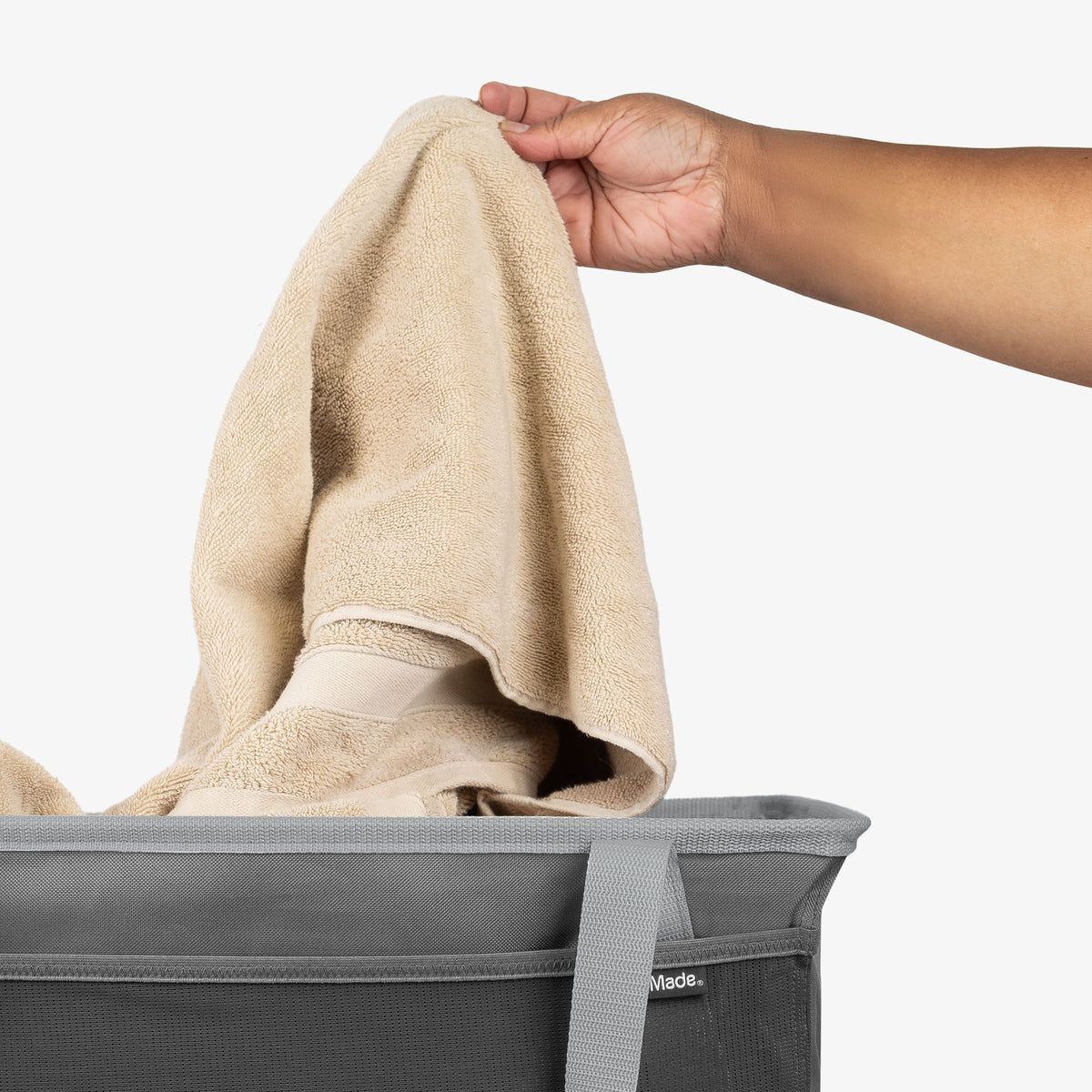 Person placing a beige towel into a gray collapsible laundry tote on a white background