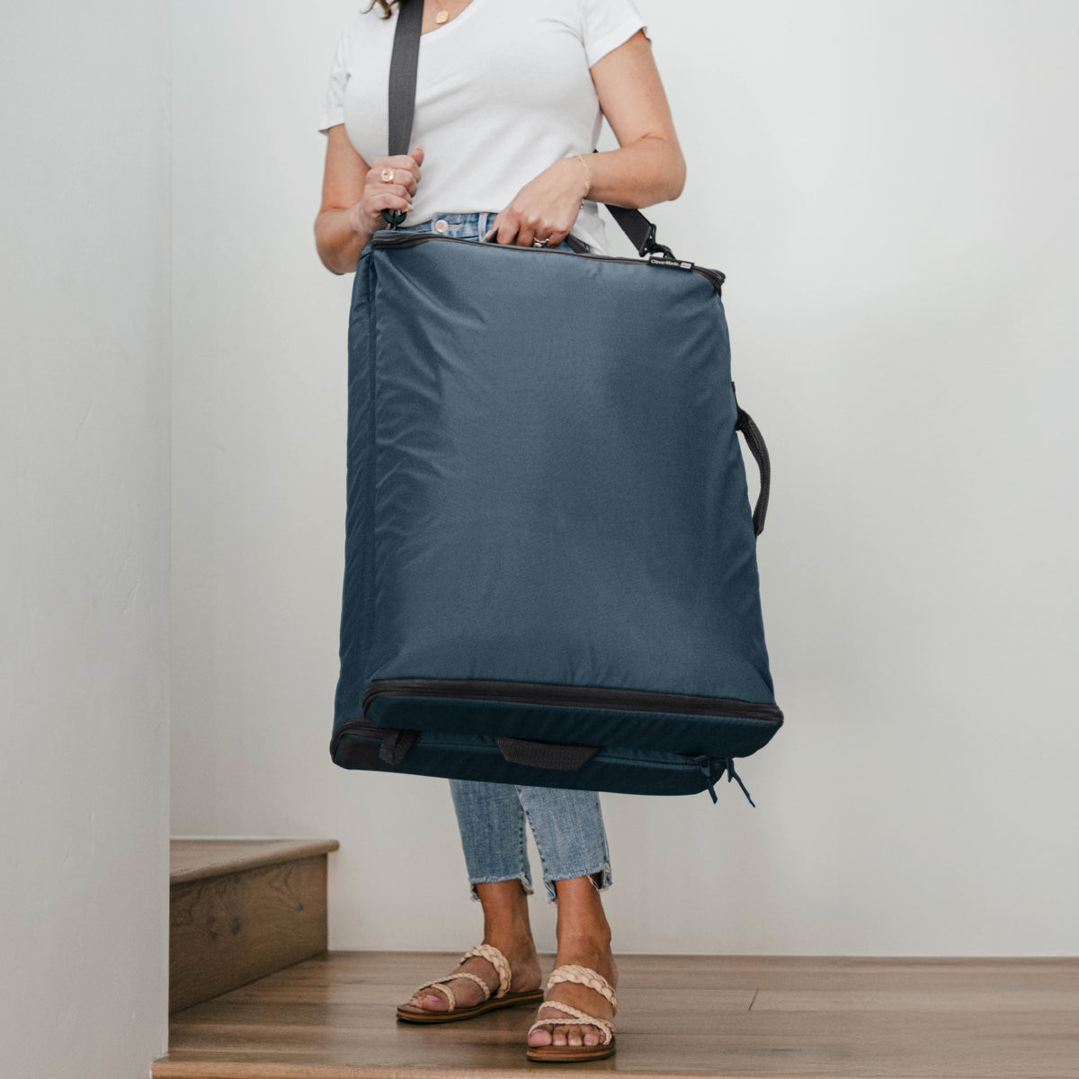 Person carrying a folded blue Convertible Laundry Hamper with a shoulder strap and a grab handle.