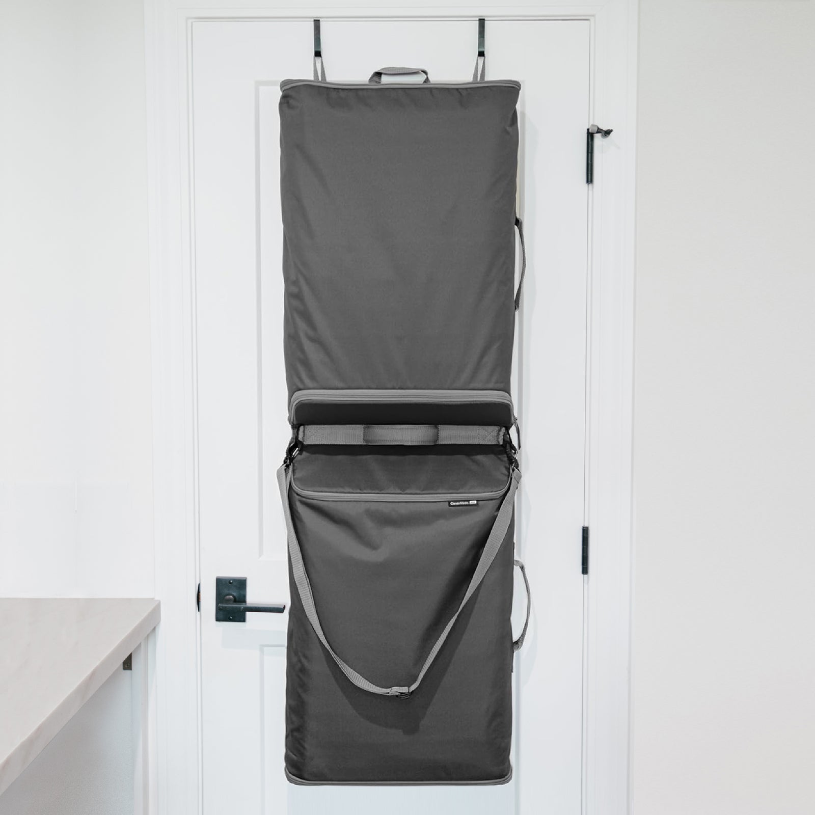A gray Convertible Laundry Hamper hanging on the back of a door with a shoulder strap and a grab handle.