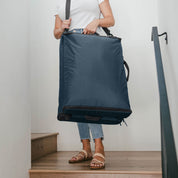 Person holding a large blue laundry bag on a wooden floor.