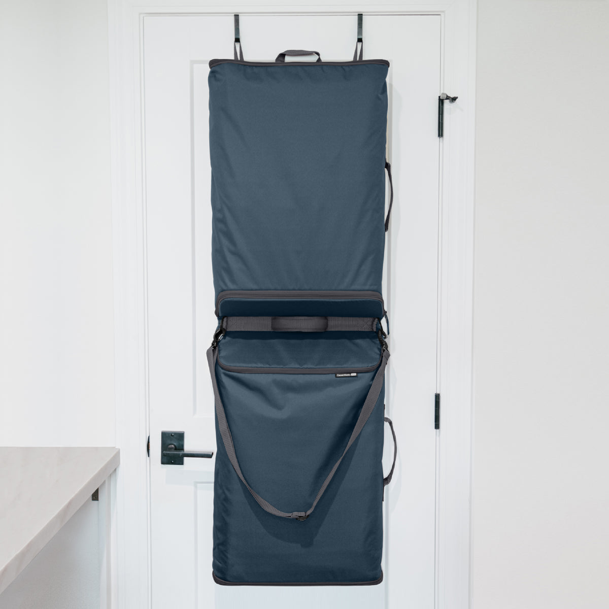 A blue Convertible Laundry Hamper hanging on the back of a door with a shoulder strap and a grab handle.