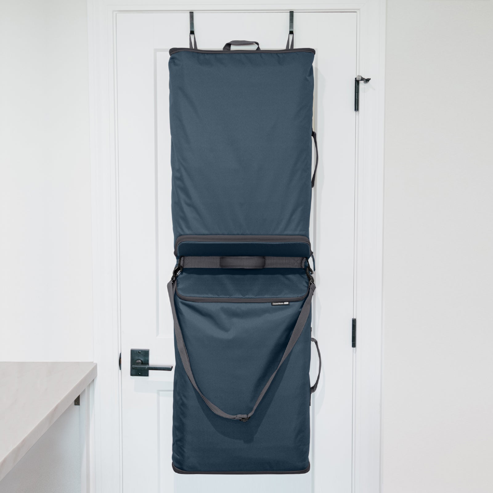 A blue Convertible Laundry Hamper hanging on the back of a door with a shoulder strap and a grab handle.
