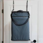 Blue over the door hamper bag with black straps hanging on a white door